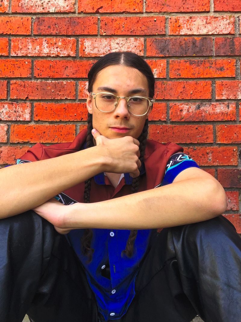 Sol, sitting against a brick wall, chin on his hand
